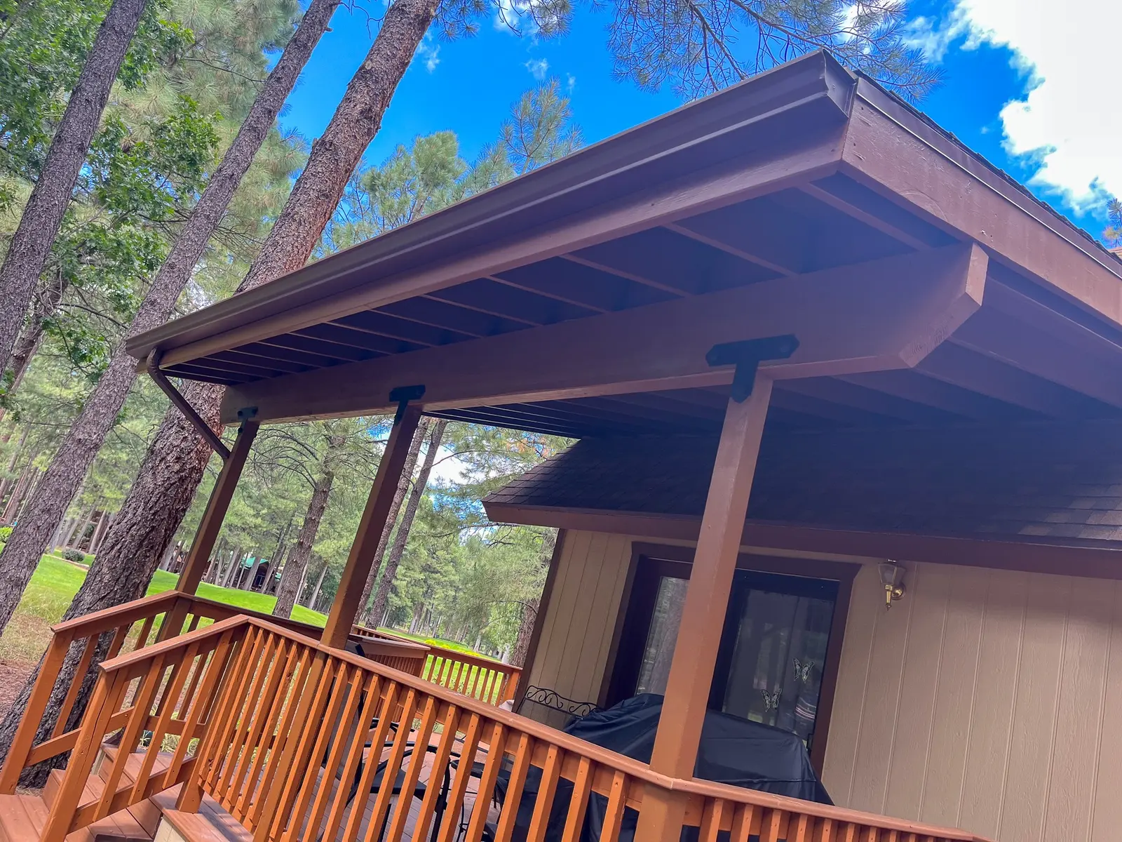 Timber covered porch with roof beams, columns and railing among pine trees